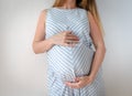 a pregnant woman in a blue dress with a white stripe, stands on a white background and holds her hands on her stomach