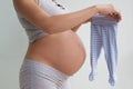 Pregnant woman chooses clothes for the baby. The pregnant woman is holding in her hands small children`s pants. Toddlers sliders. Royalty Free Stock Photo