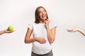 Pregnant Woman Choosing Between Apple And Donut Standing, Studio Shot Royalty Free Stock Photo