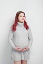 A pregnant woman with colored crimson hair in a knitted gray pullover.