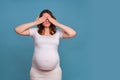 Pregnant woman covers her eyes with her hands, studio shot on blue background Royalty Free Stock Photo