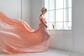 Pregnant woman dancing in pink evening dress flying on wind. Waving fabric, fashion shot.