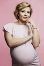 Pregnant woman in a delicate dress. Beautiful smiling blonde with a big belly on a pink background. Waiting for the birth of a Royalty Free Stock Photo