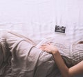 Pregnant woman in dress holding hands on belly lying on side in profile in bed.  Expectant mother waiting for baby birth during Royalty Free Stock Photo