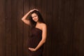 Pregnant woman in dress holds hands on belly on a dark brown background. Pregnancy, maternity, expectation concept. Beautiful tend
