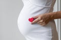 a pregnant woman in a dress holds a red heart in her hand next to a big tummy, waiting for the birth of a baby Royalty Free Stock Photo