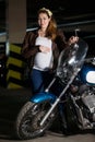 Pregnant woman dressed in brown leather jacket standing with motorcycle, holding steering wheel and her large belly Royalty Free Stock Photo