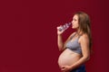 Pregnant woman drinking water from a bottle. Studio on red background young pregnant woman in sports clothes Royalty Free Stock Photo