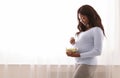 Pregnant woman eating fresh salad next to window at home Royalty Free Stock Photo