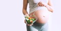 Pregnant woman eating healthy food containing folic acid, B9 vitamin. Close-up pregnant woman`s belly and vegetable salad.