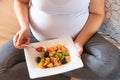 Pregnant woman eating healthy homemade organic fruit salad sitting on her bed. Royalty Free Stock Photo