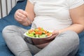 A pregnant woman is eating a healthy homemade organic fruit salad while sitting on her bed. Royalty Free Stock Photo