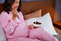 Pregnant woman eating strawberries sitting on bed at home Royalty Free Stock Photo