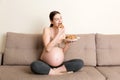 Pregnant woman enjoys eating cookies resting on the sofa at home. Unhealthy sweet pastry during pregnancy concept