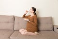 Pregnant woman enjoys eating cookies resting on the sofa at home. Unhealthy sweet pastry during pregnancy concept