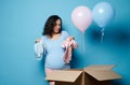 Pregnant woman, expectant mother taking out blue and pink newborn bodysuits from a cardboard box in gender reveal party Royalty Free Stock Photo