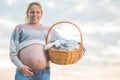 Pregnant woman expecting a baby, posing outdoors with a wicker basket with clothes for her newborn. Royalty Free Stock Photo