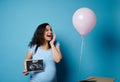 Pregnant woman experiencing joy watching a pink balloon flying out of a box, holding ultrasound scan of her future child