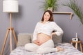 Pregnant woman experiencing lower back pain causing discomfort while she sitting on her bed at home, possibly indicating the onset Royalty Free Stock Photo
