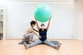 A pregnant woman with face mask sitting on a mat doing pilates exercises with a ball with the help of physiotherapist Royalty Free Stock Photo