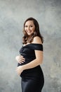 Pregnant woman in fashionable black dress smiling on gray background portrait