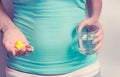 A pregnant woman first trimester in a blue T-shirt holds several medicine capsules, and in the second a glass of water. IVF. Royalty Free Stock Photo