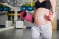 Pregnant woman at gym holding weights and mat