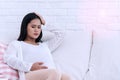 Pregnant woman with hand on forehead suffering headache and abdominal pain sitting on white sofa in the living room at home Royalty Free Stock Photo
