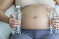 Pregnant woman hands holding pure water bottles on belly in bedroom. Royalty Free Stock Photo