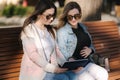 Pregnant woman with her best friend sitting in the park and looking for baby stroller using tablet. Two females in Royalty Free Stock Photo