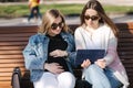 Pregnant woman with her best friend sitting in the park and looking for baby stroller using tablet. Two females in Royalty Free Stock Photo