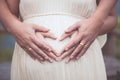 Pregnant woman and her husband making hand heart shape together