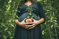 Pregnant woman holding an apple against the background of trees