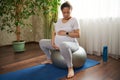 Pregnant woman holding belly, sitting barefoot on a fit ball and mat, doing breathing exercises for easy childbirth. Royalty Free Stock Photo