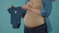 A pregnant woman holding a blue baby bodysuit, is preparing for the birth of a boy during pregnancy. Bloated belly of a Royalty Free Stock Photo