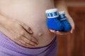 Pregnant woman holding blue baby booties on belly, closeup Royalty Free Stock Photo