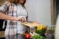 Pregnant woman holding a cutting board and pouring chopped yellow bell pepper from it into a bowl with a healthy vegetable salad, Royalty Free Stock Photo