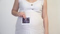 Pregnant woman holding echography picture at her belly