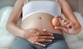 Pregnant woman holding an egg at her belly sitting on the sofa Royalty Free Stock Photo