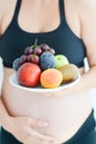 Pregnant woman holding fruits on a plate in front of her belly Royalty Free Stock Photo