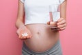 Pregnant woman holding a glass of water and pills, vitamins for pregnancy, the future mother is expecting a baby Royalty Free Stock Photo