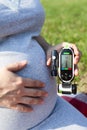 Pregnant woman holding glucometer in hand and touching her belly with other. Diabetes tests