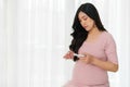 Pregnant woman holding glucose meter and checking blood sugar level by herself at home. gestational diabetes concept