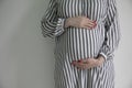 A pregnant woman holding her baby bump stood against a plain background Royalty Free Stock Photo