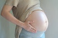 Pregnant Woman holding her right hand on her stomach takes side posture, reflective light from window to pregnant belly.