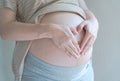 Pregnant Woman holding her right hand on her stomach takes side posture, reflective light from window to pregnant belly.