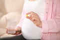 Pregnant woman holding pill and glass with water on blurred background, closeup Royalty Free Stock Photo