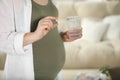 Pregnant woman holding pill and glass of water near sofa indoors, closeup Royalty Free Stock Photo