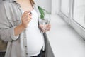 Pregnant woman holding pill and glass with water near window indoors, closeup Royalty Free Stock Photo