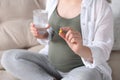 Pregnant woman holding pill and glass with water on sofa, closeup Royalty Free Stock Photo